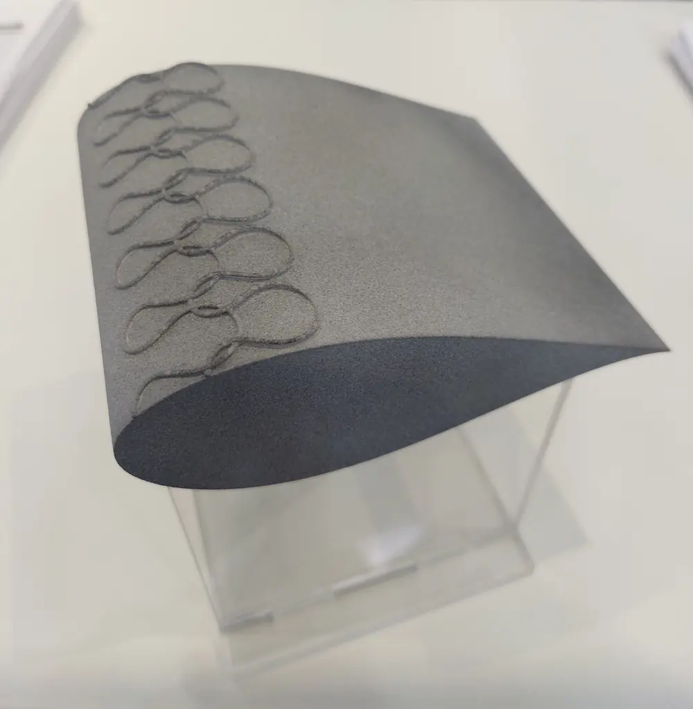 Aerodynamically shaped grey sample component with a knitted loop structure along its edge, on an acrylic stand
